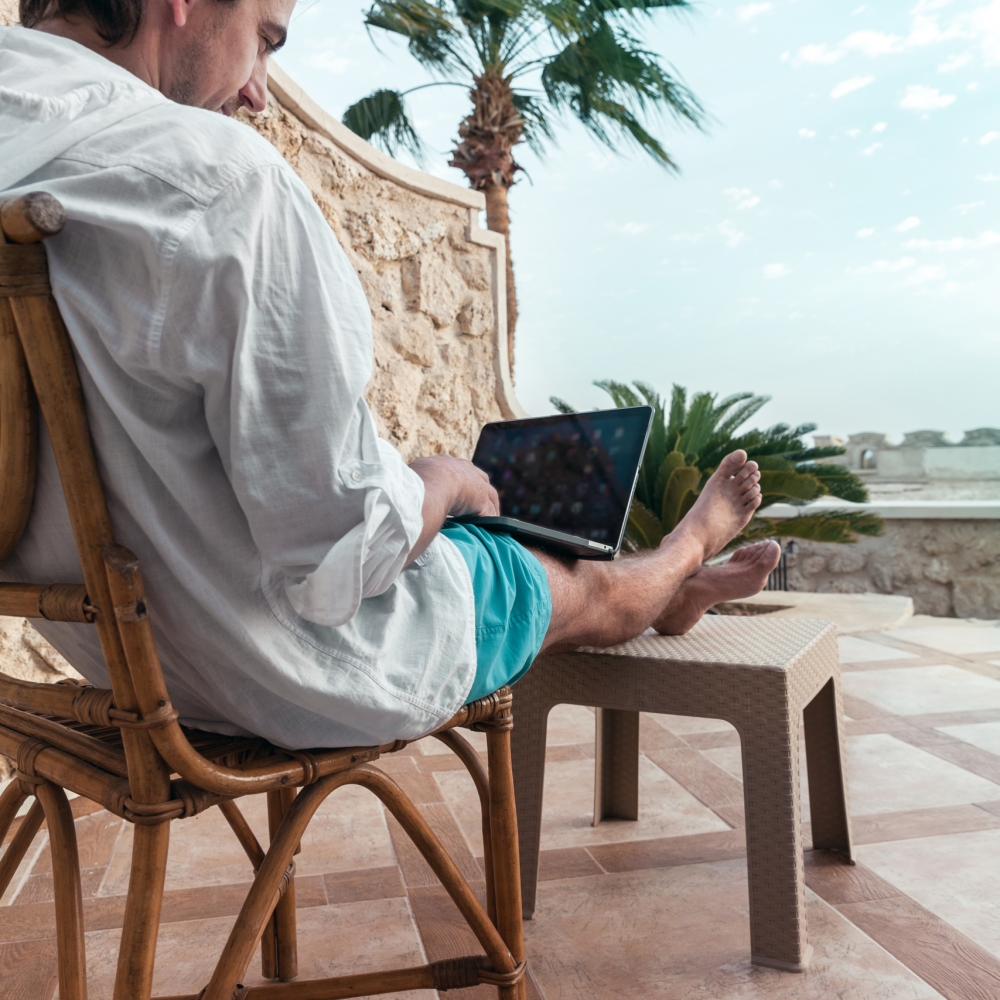 freelancer with a laptop in his hands works on vacation a man with a laptop in his hands is resting and working as a freelancer on the background of palm trees